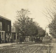 looking down dirt street with old buildings, horses and wagon