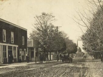 looking down dirt street with old buildings, horses and wagon