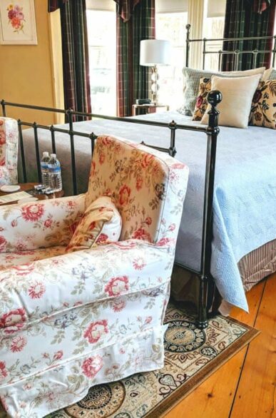 bedroom with iron bed, blue linens, two pink floral chairs